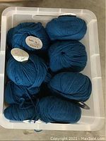 Clear container holding several skeins of dark blue colored yarn, labeled Lana
