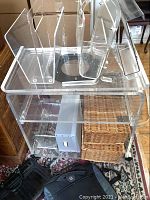 Clear acrylic cart with visible bottom shelf broken off, various acrylic and wicker baskets arranged on and inside the cart