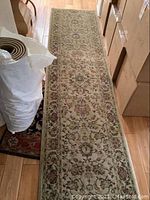 Full view of a beige floral patterned runner rug laid out on a wooden floor beside some boxes.