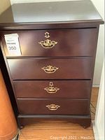 Front view of the dark brown wooden rolling file cabinet showing four drawers with ornate brass handles and a label attached to the top drawer.