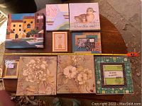 Top-down photo showing nine various framed artworks arranged on a wooden surface with a measuring tape for sizing reference.