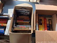 Two open boxes of assorted books showing titles related to programming, art, design, and restoration topics in hardcover and paperback.