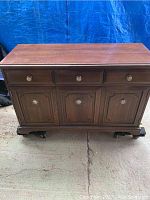 Front view of wooden buffet sideboard showing three drawers and three cabinet doors, sitting on carved bracket feet.