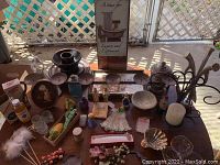 Photo showing variety of candleholders, decorative bottles, faux flowers, and knickknacks on a table.