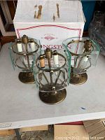 Three vintage hanging light fixtures on table with box behind them, showing brass bases and curved glass panels.