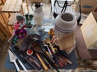 Wide view of kitchen items including large ceramic container, bottled water dispenser, wooden and plastic utensils, cutting boards, and other kitchen tools.