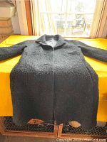 Black wool textured calf-length ladies coat laid flat showing front with sleeves and collar detail.