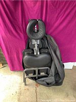 Front view of the portable massage chair showing black padded cushions and metal frame, partially covered by the carrying case.
