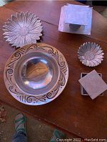 Top view of all pewter items arranged on a wooden table, showing large floral and ornamental bowls and square candle holders.