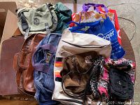 Overview of multiple bags including backpacks, leather handbags, tote bags, and reusable grocery bag showing the variety and condition.