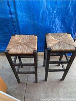 Front and top view of two wooden barstools with woven seats showing overall condition