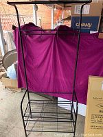 Assembled black metal coat and shoe rack with wire shoe shelf and hanging rod, showing some dust and visible hooks for coats