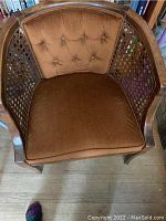 Frontal view of chair showing brown velvet tufted upholstery on the backrest and seat cushion, with open cane weave wooden sides.