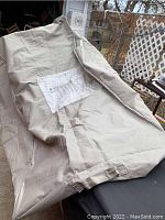 A photo showing a light beige, large grill cover made of sturdy fabric, unwrapped and laid out with attached product label.