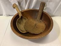 Large round wooden butter bowl with two wooden paddles inside on white background.