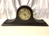 Front view of vintage wooden mantel clock with rounded top and dark wood finish.