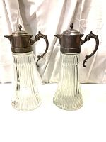 Two vintage glass decanters with silver plated zinc lids and handles, standing side by side showing entire items.