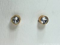 Front view of two round clear Swarovski crystal stud earrings set in gold-tone rhodium plated metal.