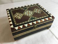 Top and side views showing rectangular jewelry box with intricate multi-wood geometric inlay patterns and bone borders.