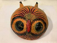 Top view of vintage papier mache wild cat mask showing front face with stylized features in black and red paint on orange base, small ears.