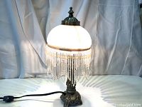 Front view of the vintage lamp showing lit frosted glass shade and beaded fringe.