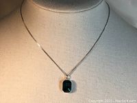 Full view of the necklace on display stand, showing the green crystal pendant hanging on the silver Cuban chain.