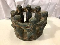 Front view of the pottery sculpture showing eight figures joined in a circle, arms around shoulders.