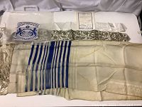 Prayer shawl with blue stripes and knotted fringes laid on table, showing discoloration and wear.