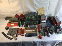 Overview of lot showing assortment of vintage HO scale model train parts including buildings, trees, track section, landscape base, and vehicles.