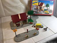 Photo showing the full set including bank building, road base, tree, street lamps, flower planters, figurines, and yellow postal vehicle with box and box art in background.