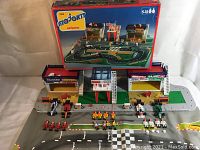 Wide view of the complete set including box, race track mat, buildings, cars, figurines, and accessories.