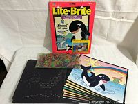 Photo showing Lite-Brite box with themed picture templates, bag of colored pegs, and peg screen laid out.