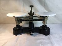 Full view of the antique balance scale showing the black metal base, central adjustment knob, and two white weighing plates