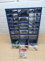 Front view of blue plastic organizer showing small and larger drawers with various hardware inside