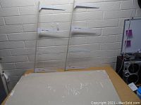 The shelving unit mounted on a wall with four white shelves attached to vertical metal brackets.