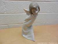 Full view of Lladro figurine of girl with angel wings, standing with hands behind back in long dress.