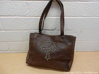 Front view of the brown leather purse showing the silver studded cross design on the front side.