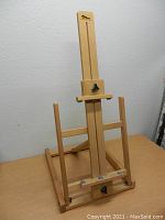 Front view of wooden easel showing adjustable vertical track with black thumb screw, base and frame visible.