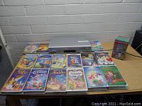 Sony VHS player with 14 Disney VHS movie tapes and 1 boxed classic Christmas movie set arranged on a table.