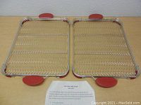 Pair of stainless steel Silpan cooling racks with red silicone grip handles shown flat on table top.