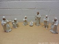 Wide view of seven nativity porcelain figurines arranged on table in front of brick wall
