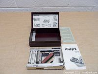 Vintage Allegro shaving razor sharpener device inside open fitted case with manuals and instruction sheet visible on a wooden surface.