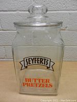 Front view of the large clear glass Seyfert's Butter Pretzels jar, showing printed logo and text on jar.