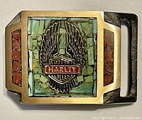 Front view of vintage brass Harley Davidson belt buckle featuring turquoise and red stone inlays with winged Harley logo