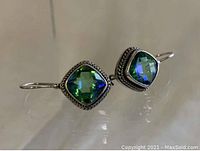 Close-up of front of earrings showing cushion-cut blue-green faceted stones set in sterling silver with rope detailing.