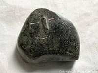 Front view of the dark stone abstract smiling face carving showing the facial features and stone texture.