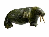 Side view of a green stone walrus sculpture with ivory tusks, showing carving detail and polish.