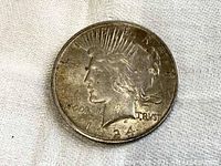 Obverse side of a 1924 Peace Dollar coin showing Lady Liberty wearing a radiate crown, date 1924, and partial inscriptions 'IN GOD WE TRUST'. Coin surface is worn with visible tarnish.