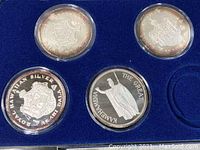 Four silver coins secured in plastic capsules on blue felt display, showing both front and back details.