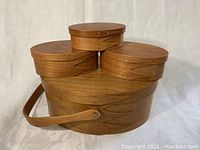 Four oval wooden Shaker pantry boxes nested together, largest has a handle, natural wood finish